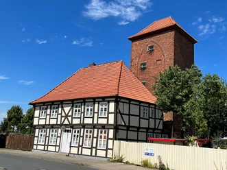 Fachwerkhaus und ein beeindruckender alter Wehrturm nebeneinander an einem sonnigen Tag.