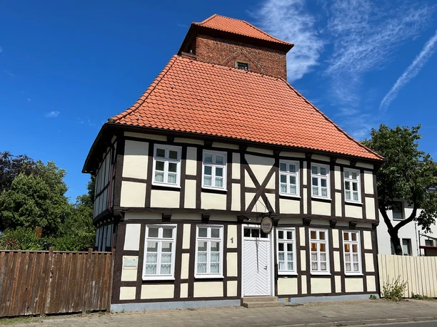 Fachwerkgebäude mit rotem Ziegeldach und gemauertem Turm in Verden unter klarem, blauem Himmel.