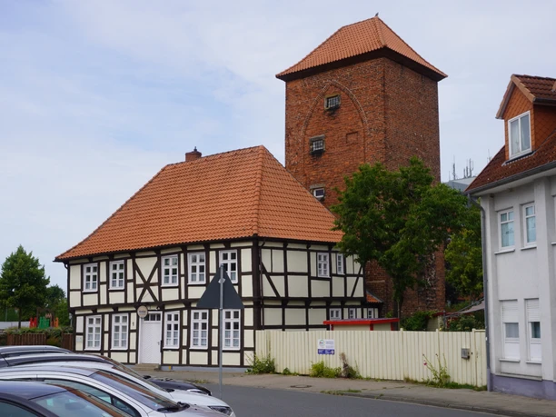 Wehrturm in Verden mit historischem Fachwerkhaus im Vordergrund, rotes Ziegeldach, klare Himmelsszene.