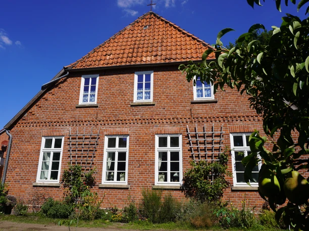 Backsteinfassade der Alten Schule in Dauelsen mit gepflegtem Garten, Fenster mit weißen Sprossen.