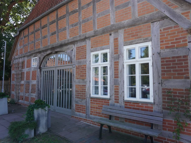 A half-timbered building with red bricks, wooden beams, and an entrance area near the bank; three white windows.