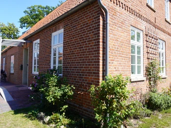 Dauelsen Alte Schule Rotes Backsteinhaus mit mehreren weißen Sprossenfenstern, teils von Grünpflanzen umgeben.