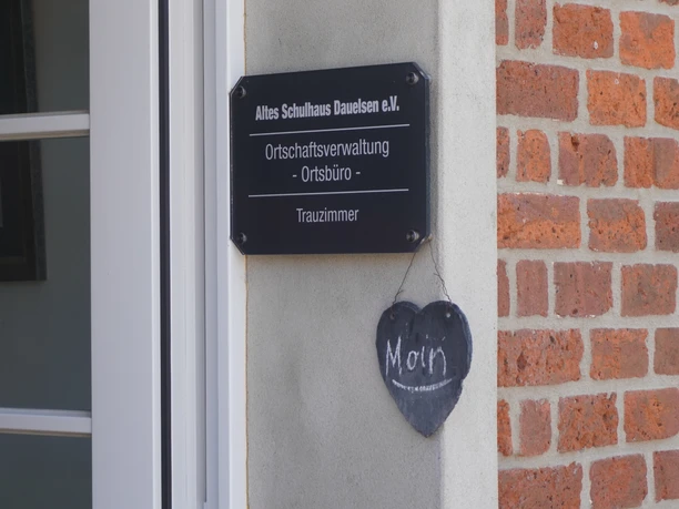 Dauelsen Alte Schule Schild "Altes Schulhaus Dauelsen e.V." an einer Backsteinwand, daneben ein kleines Herzhängerchen.