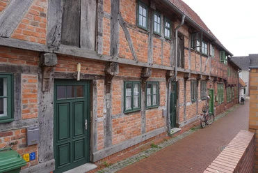 Fachwerkhäuserzeile aus rotem Backstein in Verden, mit grünen Türen und Fenstern an einer gepflasterten Straße.