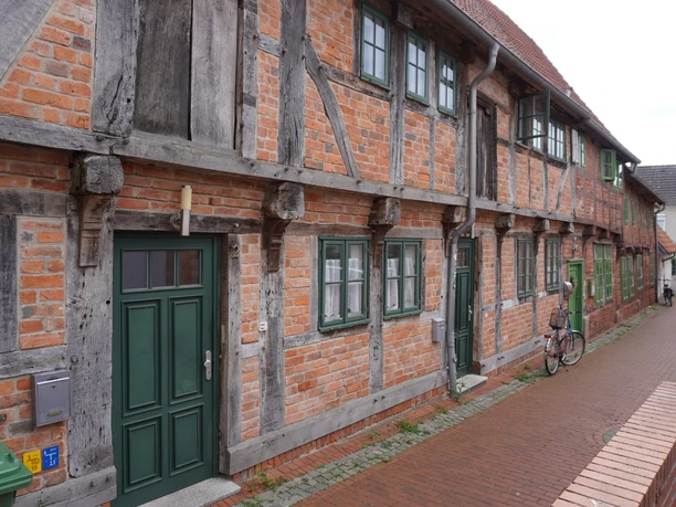 Budenhäuser Verden Fachwerkhäuserzeile aus rotem Backstein in Verden, mit grünen Türen und Fenstern an einer gepflasterten Straße.