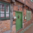Fachwerkhäuser mit roten Ziegelwänden, weißen Fenstern und grünen Türen entlang einer Pflastergasse.