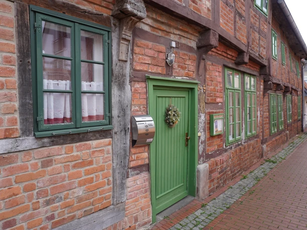 Fachwerkhäuser mit roten Ziegelwänden, weißen Fenstern und grünen Türen entlang einer Pflastergasse.