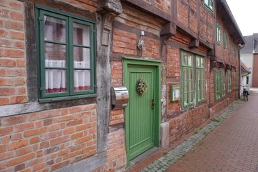 Budenhäuser Verden Fachwerkhäuser mit roten Ziegelwänden, weißen Fenstern und grünen Türen entlang einer Pflastergasse.