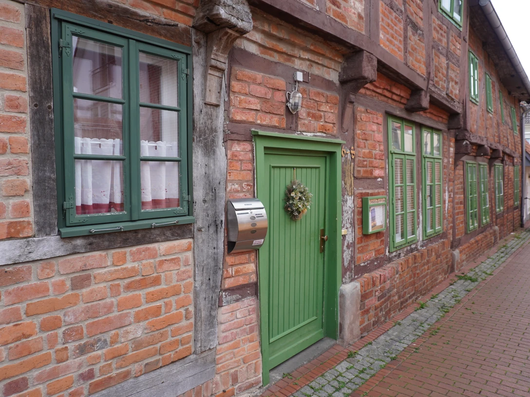 Budenhäuser Verden Fachwerkhäuser mit roten Ziegelwänden, weißen Fenstern und grünen Türen entlang einer Pflastergasse.