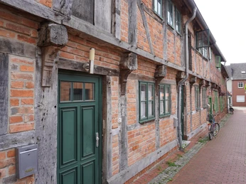 Budenhäuser Verden Fachwerkhäuser in einer ruhigen Gasse mit Backsteinfassade, grünen Fenstern und einer Haustür.