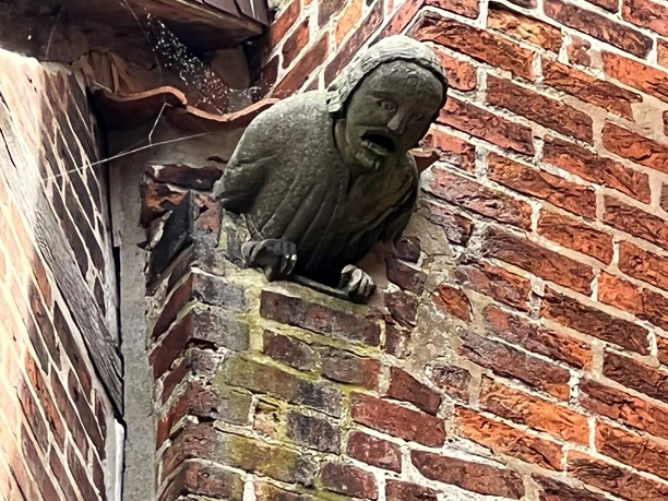 Steinerner Mann Verden Steinerne Skulptur eines schreienden Gesichts mit langen Haaren ragt aus der Backsteinwand hervor.