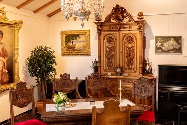 Heimatmuseum Antiker Speisesaal mit Holzstühlen, geschnitztem Schrank und Gemälden an den Wänden.