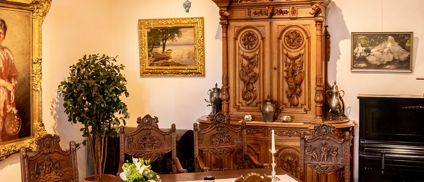 Heimatmuseum Antiker Speisesaal mit Holzstühlen, geschnitztem Schrank und Gemälden an den Wänden.