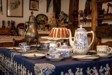 Heimatmuseum Ein gedeckter Tisch mit blau-weißem Porzellan, einer Kaffeekanne und einem Gugelhupf im Vintage-Stil.