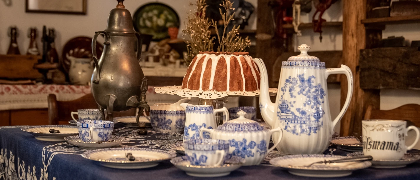 Heimatmuseum Ein gedeckter Tisch mit blau-weißem Porzellan, einer Kaffeekanne und einem Gugelhupf im Vintage-Stil.