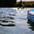 Stand-up-Paddling Nahaufnahme eines blauen SUP-Boards auf einem ruhigen See mit glitzerndem Wasser und unscharfen Ufern.