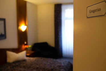 Hotel & Restaurant Klosterkrug - Zimmer Gregorius Großzügiges Hotelzimmer mit einem Doppelbett, weichen Kissen, stilvollem Sessel und warmem Licht.