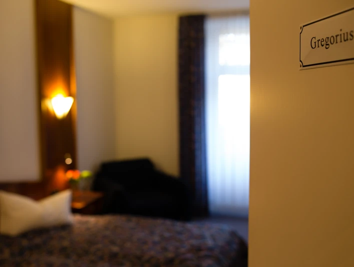 Hotel & Restaurant Klosterkrug - Zimmer Gregorius Großzügiges Hotelzimmer mit einem Doppelbett, weichen Kissen, stilvollem Sessel und warmem Licht.