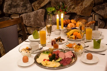 Hotel & Restaurant Klosterkrug - Frühstück Ein opulent gedeckter Frühstückstisch mit Wurst, Käse, Brot, Saft und Kerzenlicht.