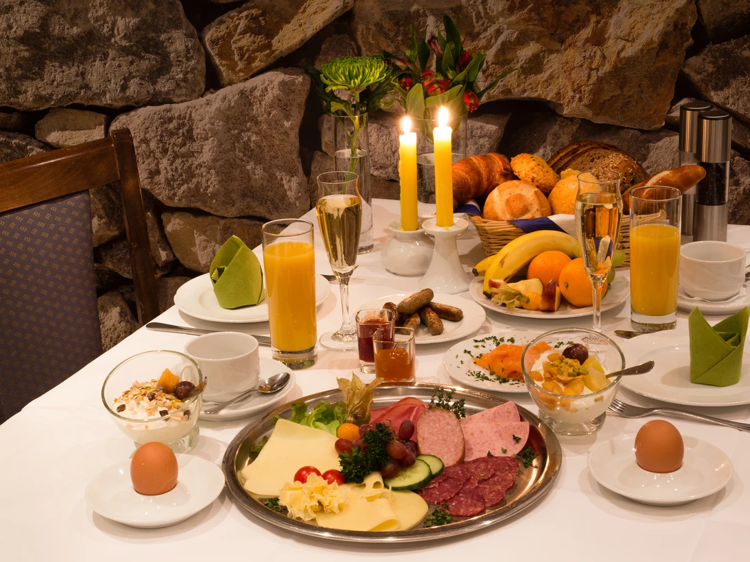 Hotel & Restaurant Klosterkrug - Frühstück Ein opulent gedeckter Frühstückstisch mit Wurst, Käse, Brot, Saft und Kerzenlicht.
