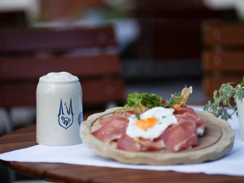 Hotel & Restaurant Klosterkrug - Restaurant Ein Tisch mit Bierkrug und einem hölzernen Teller, belegt mit Schinken, Gemüse und Garnitur.