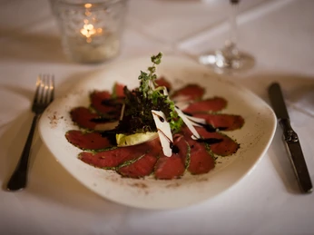 Hotel & Restaurant Klosterkrug - Restaurant Ein Teller mit dünn geschnittenem Rindercarpaccio, garniert mit Salat und Balsamico-Glasur.