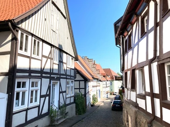La Petite Maison Fachwerkhäuser säumen eine gepflasterte Straße unter klarem, blauem Himmel in einer malerischen Altstadt.