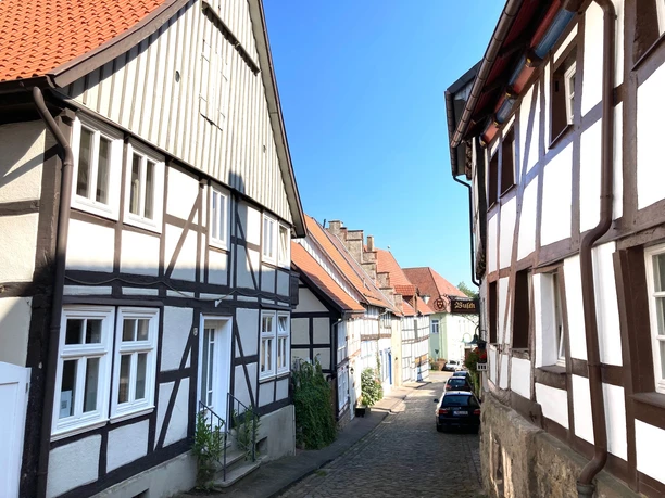 La Petite Maison Fachwerkhäuser säumen eine gepflasterte Straße unter klarem, blauem Himmel in einer malerischen Altstadt.
