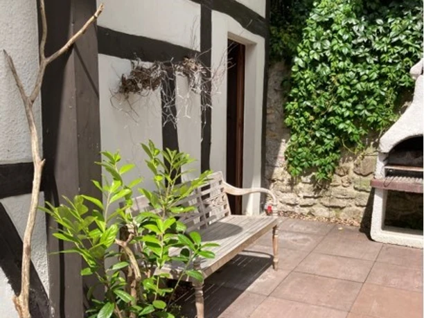 La Petite Maison - Innenhof Ein kleiner Innenhof mit Topfpflanzen, einer Holzbank und einem gemauerten Grill.