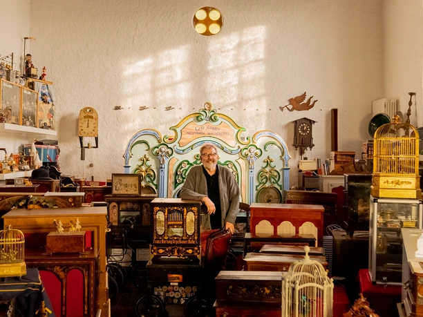 Drehorgelmuseum Ein Mann steht in einem Raum voller antiker Drehorgeln und Uhren, umgeben von nostalgischem Dekor.