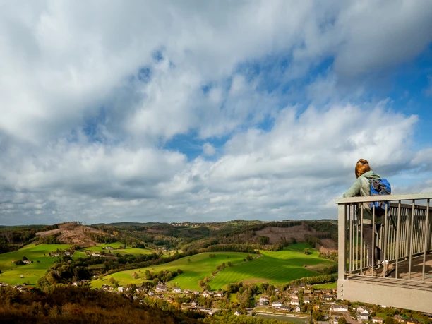 Skywalk Morsbach Person mit Rucksack auf Aussichtsplattform blickt über eine weitläufige, grüne Hügellandschaft.