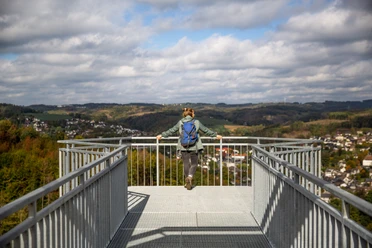 Skywalk Morsbach Frau mit blauem Rucksack genießt von Aussichtsplattform einen weiten Blick über bewaldete Hügel.