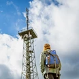 Aussichtsturm Hohe Hardt Person mit Rucksack betrachtet bei bewölktem Himmel einen hohen Sendemast aus Metall.