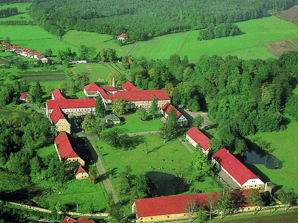 Landesvolkshochschule Hardehausen - Luftaufnahme Luftaufnahme eines Gebäudekomplexes mit roten Dächern, umgeben von Wäldern und Wiesen.