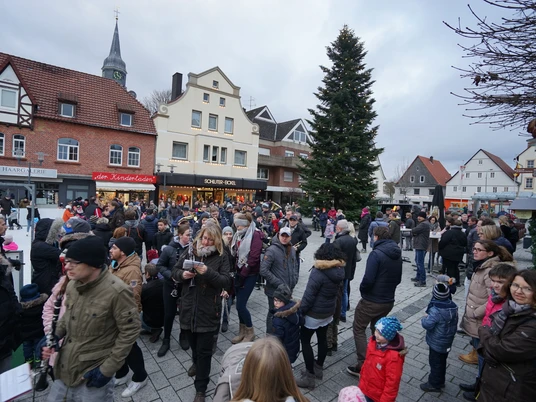 Menschen versammeln sich um einen großen Tannenbaum auf einem belebten Weihnachtsmarkt.