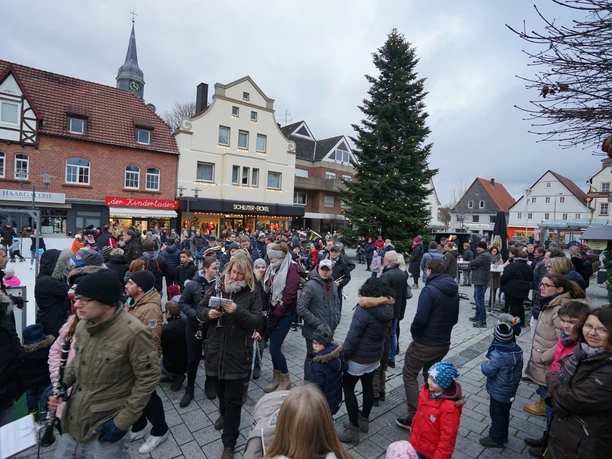 DSC00610.JPG Menschen versammeln sich um einen großen Tannenbaum auf einem belebten Weihnachtsmarkt.