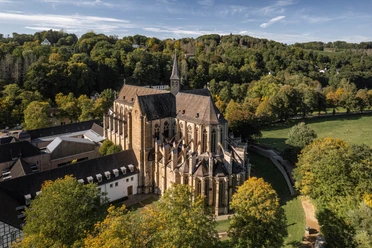 Altenberger Dom Luftaufnahme einer historischen Kirche inmitten grüner Landschaft und Bäumen, umgeben von Hügeln.