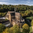 Altenberger Dom Luftaufnahme einer historischen Kirche inmitten grüner Landschaft und Bäumen, umgeben von Hügeln.