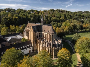 Altenberger Dom Luftaufnahme einer historischen Kirche inmitten grüner Landschaft und Bäumen, umgeben von Hügeln.