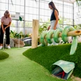 Adventuregolf Zwei Frauen spielen Minigolf in einer Indooranlage mit natürlichen Elementen und viel Grün.