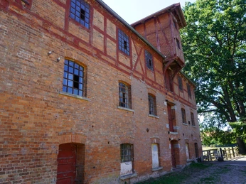 Eitzer Mühle Backsteinmühle mit Fachwerk, großen Fenstern in grüner Umgebung aus Bäumen und gemustertem Himmel.