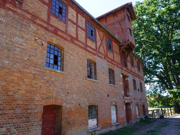 Eitzer Mühle Backsteinmühle mit Fachwerk, großen Fenstern in grüner Umgebung aus Bäumen und gemustertem Himmel.