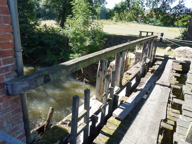 Eitzer Mühle Eine alte Wassermühle mit hölzernem Steg, umgeben von Bäumen; Wasser fließt unter der Brücke.