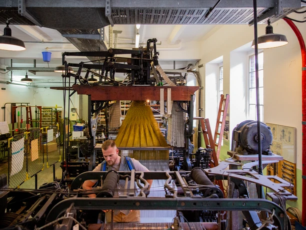 Wülfing Museum Ein Mann arbeitet in einer traditionellen Textilfabrik mit alten Webstühlen und industrieller Atmosphäre.