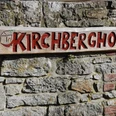 Kirchberghof Herlinghausen Holzschild mit roter Aufschrift "Kirchberghof" hängt an einer groben Steinmauer.