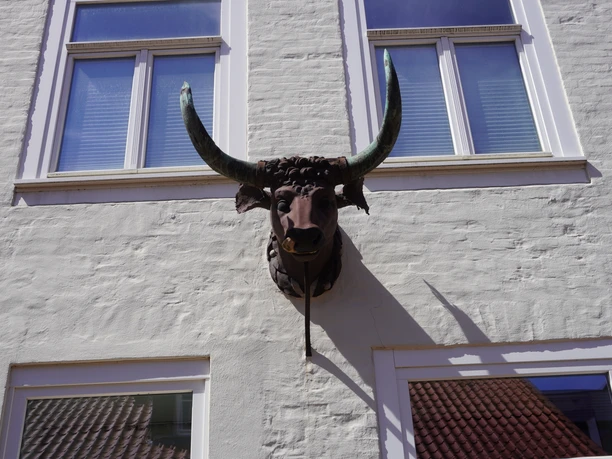 A bronze sculpture of a bull's head with imposing horns adorns the facade of a whitewashed building.