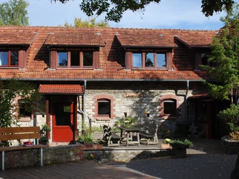 Kirchberghof Herlinghausen - Innenhof Ein sonniger Innenhof mit Steinmauern, roten Dachziegeln und einem rustikalen Holz-Tischensemble.