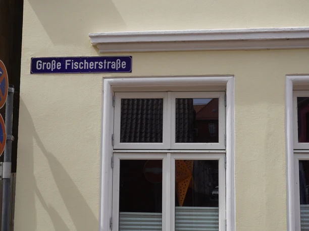 Straßenschild "Große Fischerstraße" an einer hellen Hauswand mit Fenstern im Sonnenschein.