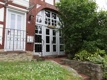 Kirchberghof Herlinghausen - Die Villa Eingang einer Fachwerkvilla mit weißen Fenstern, umgeben von grünen Büschen und einem kleinen Weg.