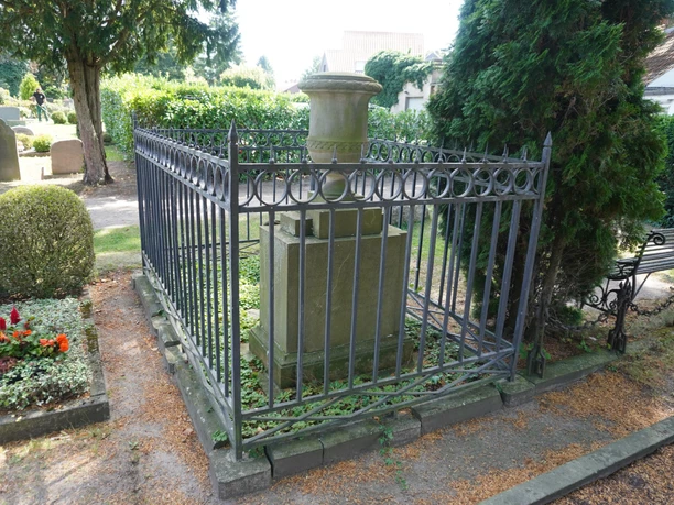 Goldmann's grave, surrounded by a wrought-iron fence in a peaceful cemetery.